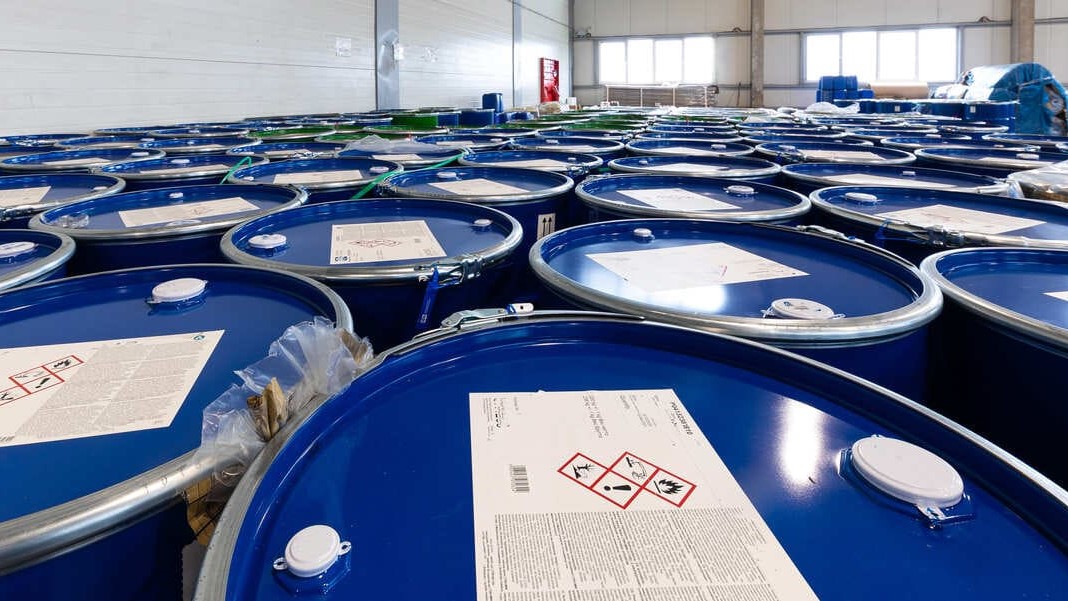 Almacenamiento correcto de bidones de disolventes halogenados en nave industrial con pictogramas de peligrosidad.
