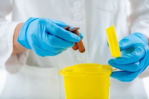 Técnico de laboratorio depositando viales en contenedor amarillo de residuos biosanitarios peligrosos.