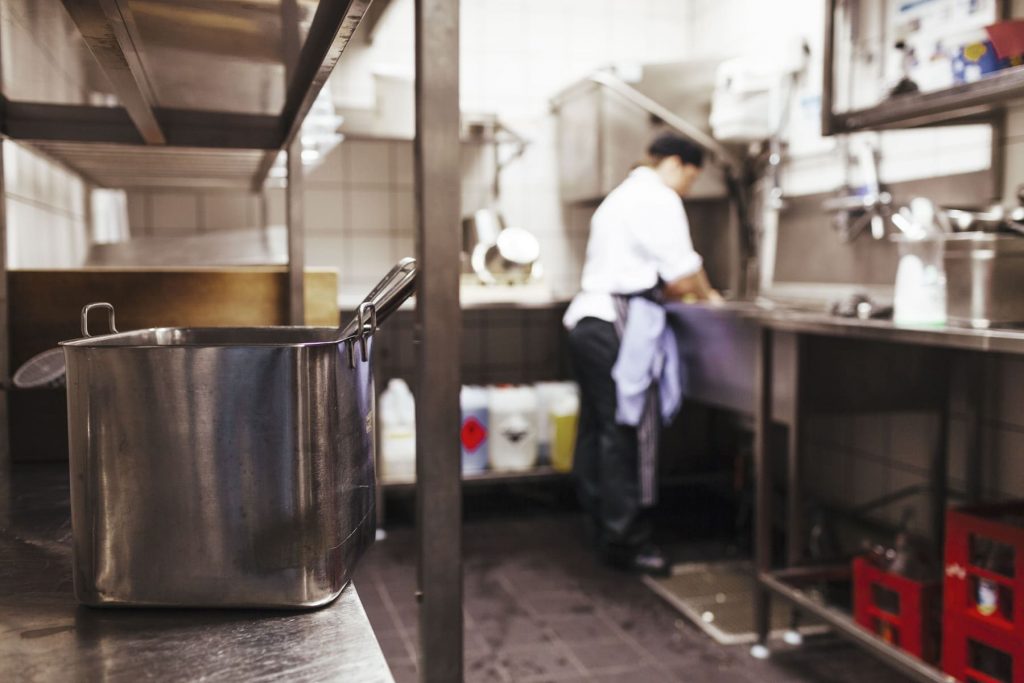 Personal de cocina en restaurante descartando aceite vegetal usado en contenedor especializado de gestión de residuos.