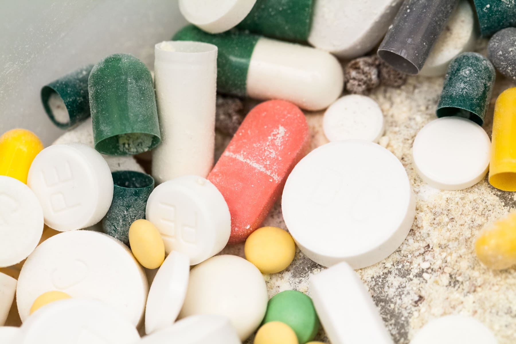 Variedad de medicamentos caducados y fuera de especificación: comprimidos blancos, cápsulas amarillas, verdes y rojas, junto con frascos de diferentes colores listos para gestión de residuos farmacéuticos.