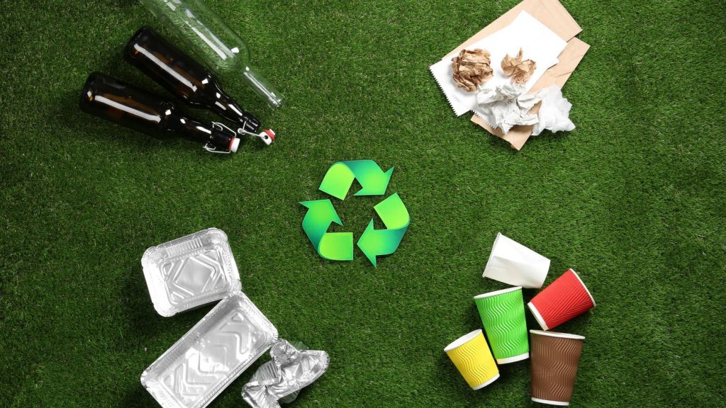 Símbolo de reciclaje rodeado de vidrio, papel, aluminio y vasos separados por tipo.